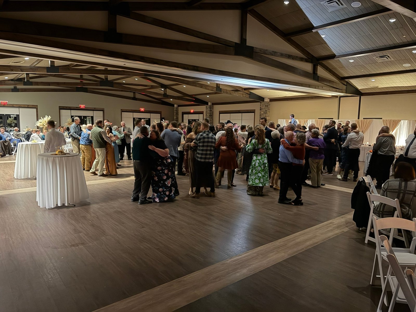 Couples dancing on a wooden dance floor in a spacious, modern event hall with vaulted ceilings.