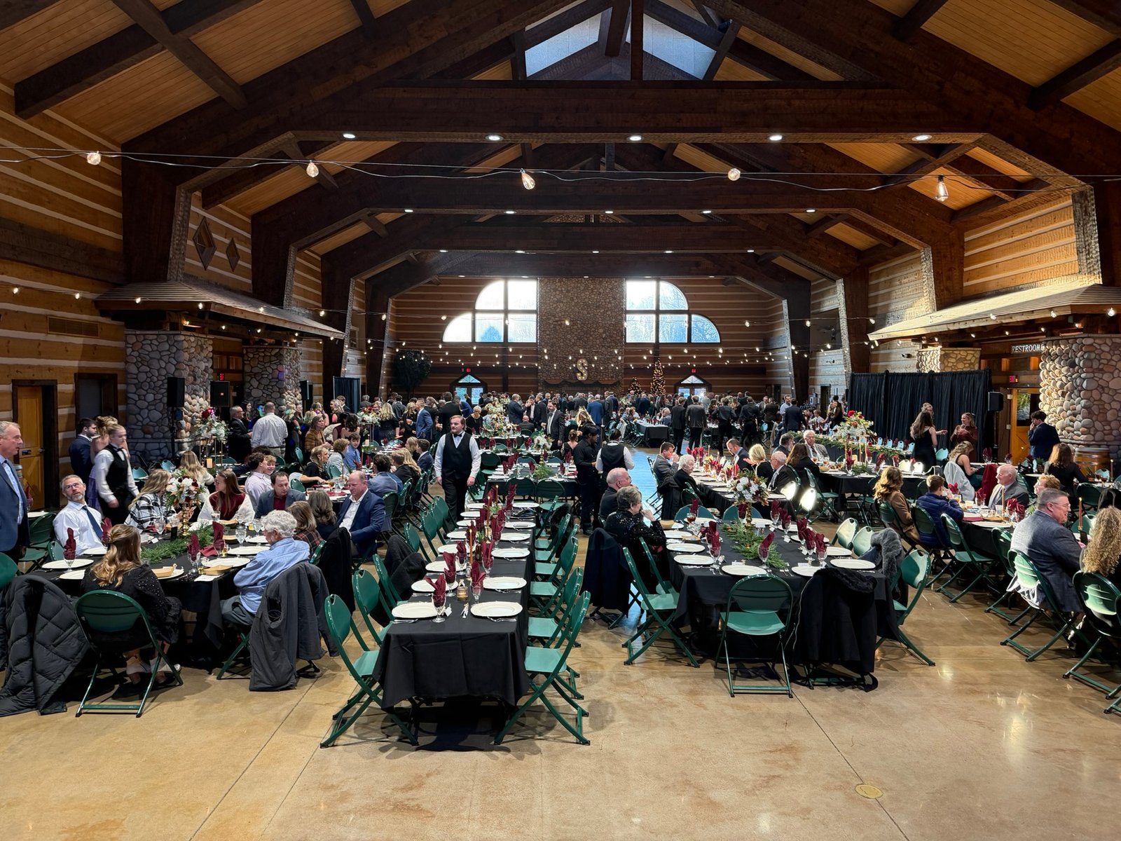 A banquet hall with wood beam ceilings and stone features, filled with guests seated at long tables for an event.