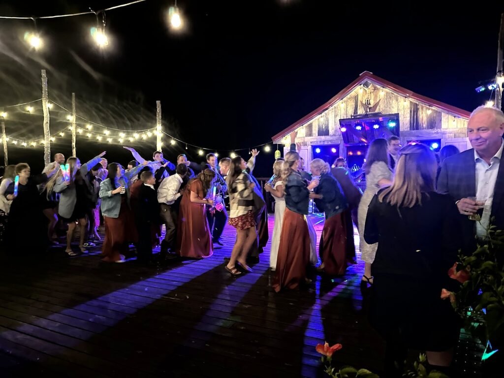 People dancing on a wooden deck at night under string lights with a barn in the background