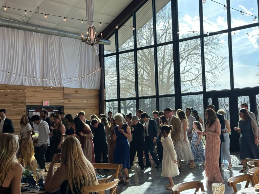 Burdoc Farms Wedding DJ | Crofton KY Wedding DJ & MC 15 Guests in semi-formal attire socialize in a bright room with floor-to-ceiling windows and wooden walls