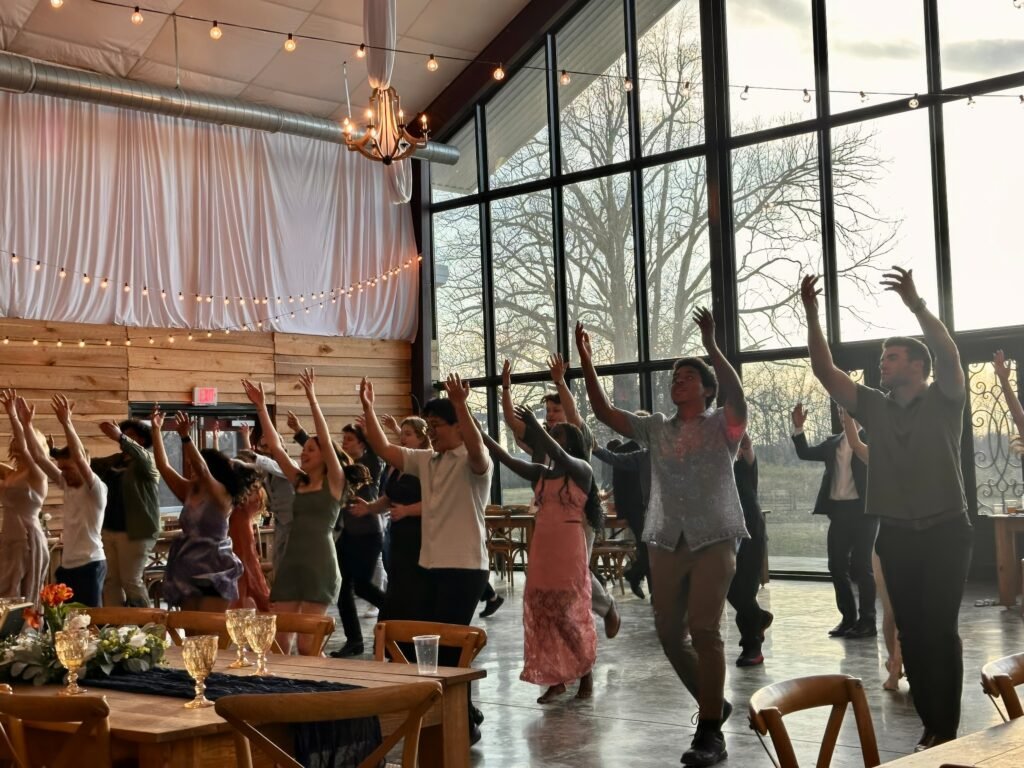 Burdoc Farms Wedding DJ | Crofton KY Wedding DJ & MC 2 Guests dancing with their arms raised in a bright event space with large windows and string lights