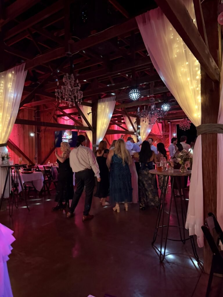 Guests dancing under red uplighting in the barn at a Farmer & Frenchman wedding reception near Henderson, KY