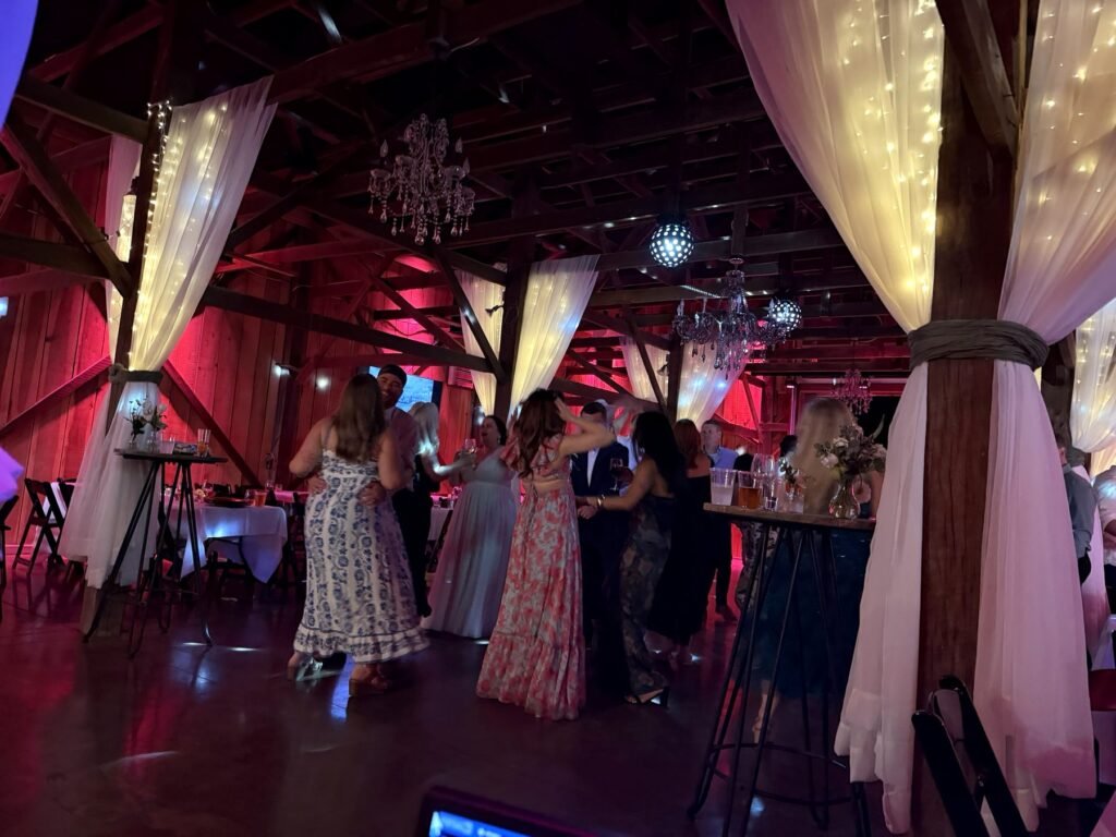 Guests celebrating in the Farmer & Frenchman barn with white drapes, chandeliers, and red uplighting near Henderson, KY
