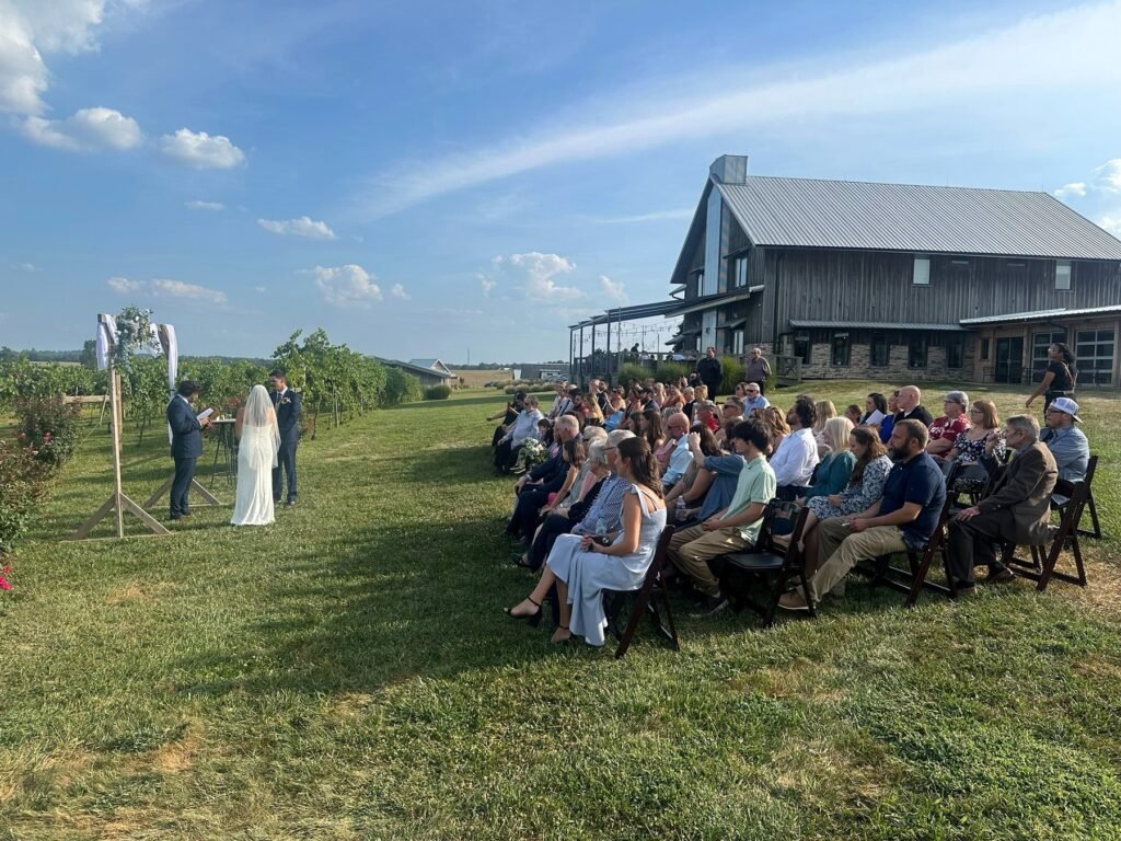 Outdoor lawn wedding ceremony with the vineyard and barn in view at Farmer & Frenchman near Henderson, KY