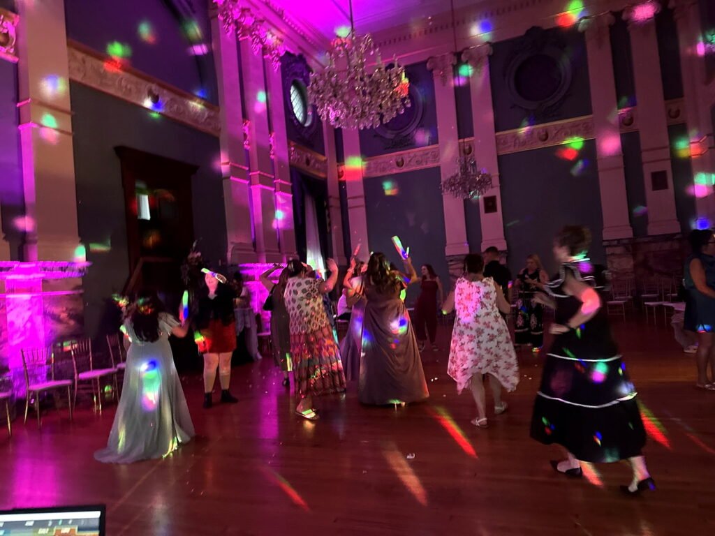Guests dancing in an ornate ballroom illuminated by purple light and colorful disco spots