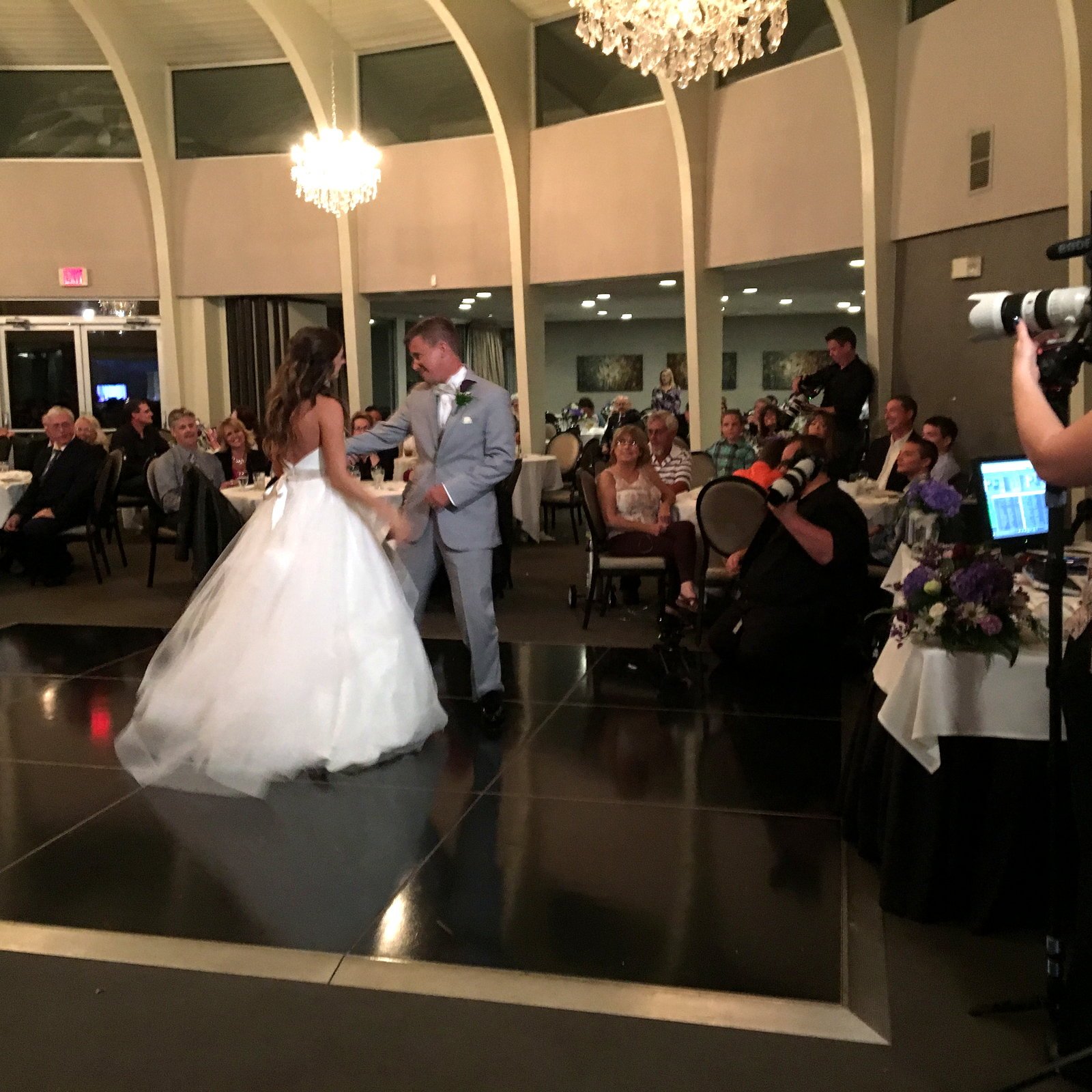 Bride in a white gown and groom in a grey suit dancing on a black dance floor at their wedding reception