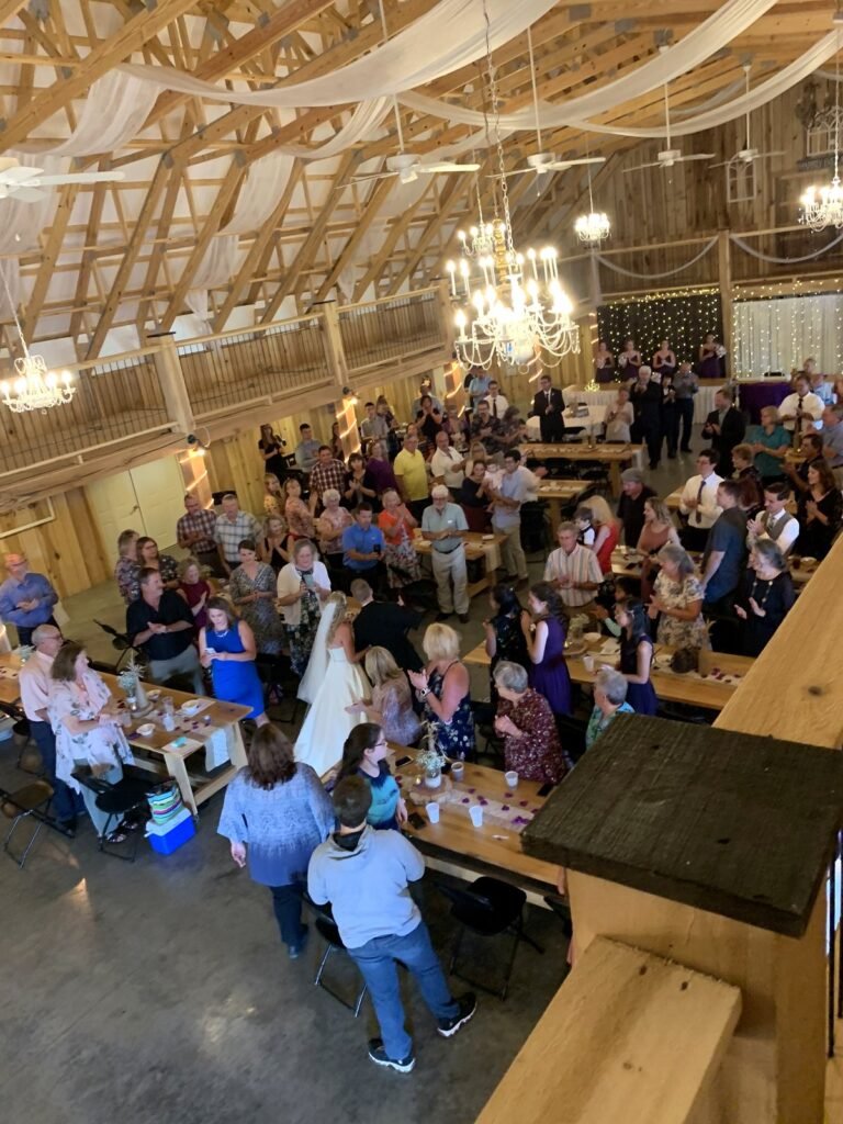 Wedding ceremony in a rustic barn with guests gathered around a bride and groom
