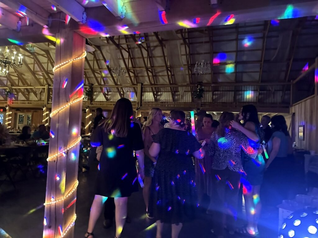 People dancing in a rustic barn illuminated by colorful disco lights and warm string lights