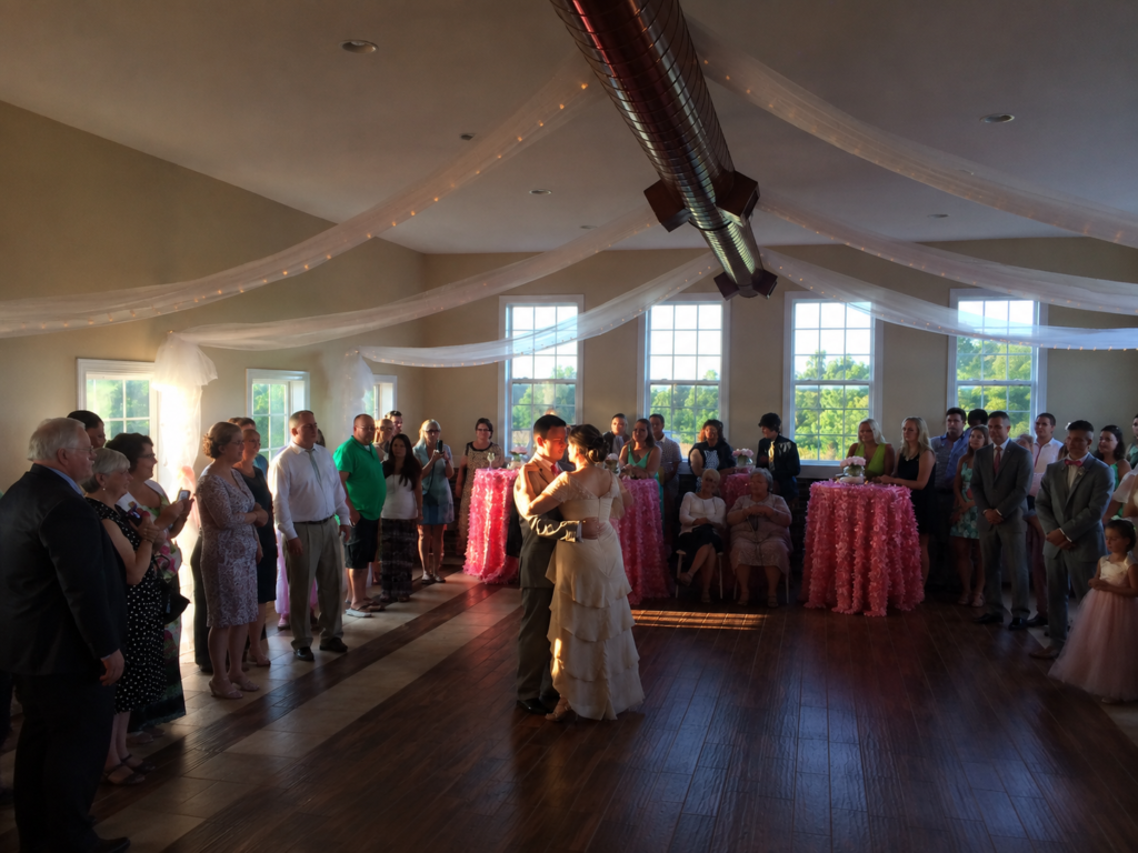 A bride and groom share a first dance, surrounded by guests at a wedding reception.