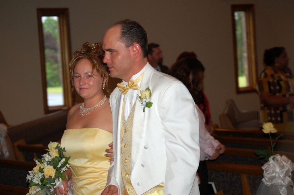 Bride in a yellow strapless gown and groom in a white tuxedo with yellow accents standing together.