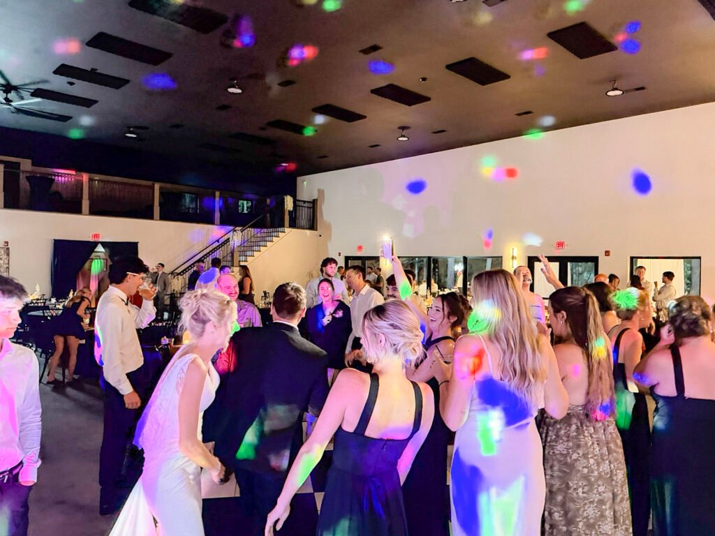 Guests in formal attire dancing under colorful lights at a Highbanks wedding reception.