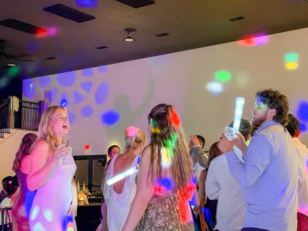 Wedding guests dancing with foam glow sticks under colored lights at Highbanks.