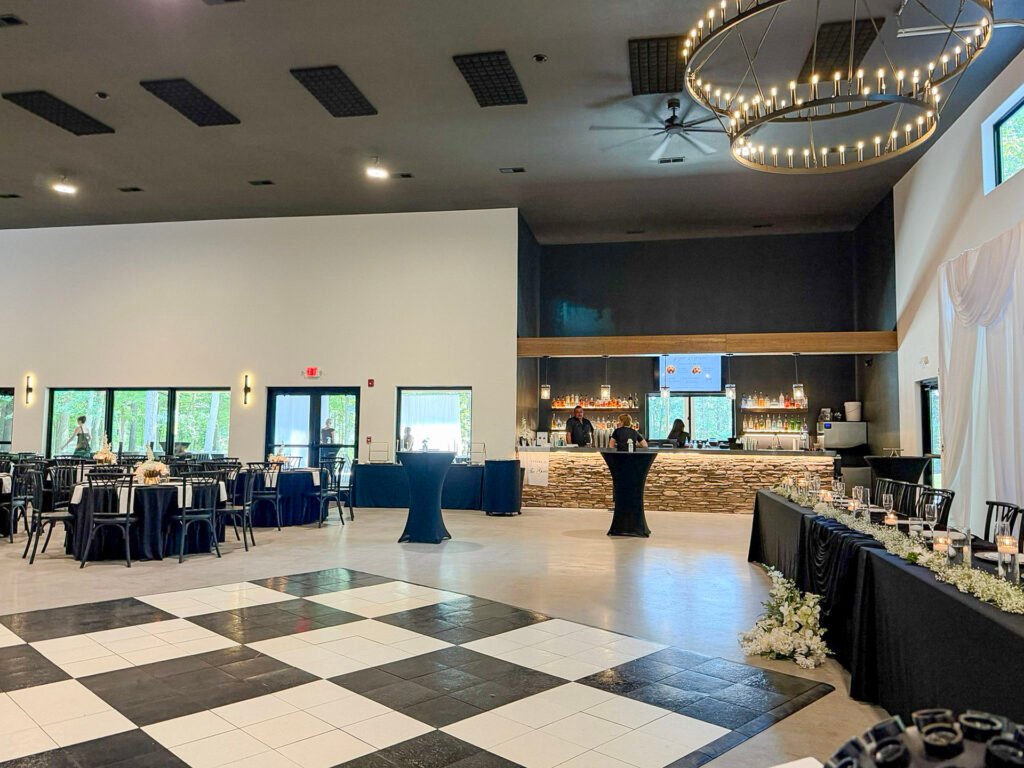 Event space at Highbanks Wedding & Events with a black and white checkered dance floor, black-linen tables and a stone-faced bar.